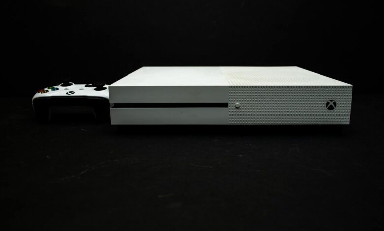 Close-up of a white gaming console with a black controller on a dark background.