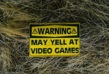A funny yellow warning sign on grass reading 'Warning May Yell at Video Games'.