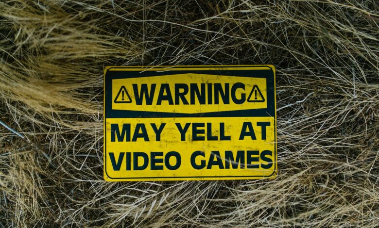 A funny yellow warning sign on grass reading 'Warning May Yell at Video Games'.