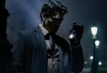 A man in dark clothing holds a pocket watch on a dimly lit street at night.