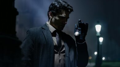 A man in dark clothing holds a pocket watch on a dimly lit street at night.