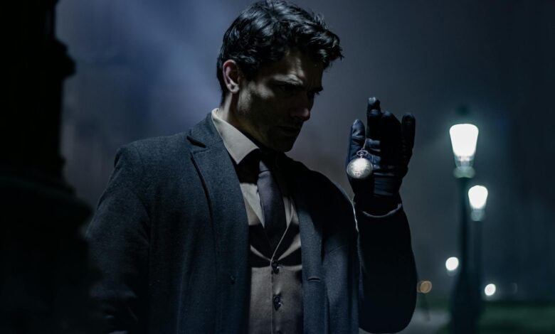 A man in dark clothing holds a pocket watch on a dimly lit street at night.