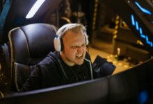 A passionate gamer celebrating victory while gaming indoors with white headphones and a gaming chair.