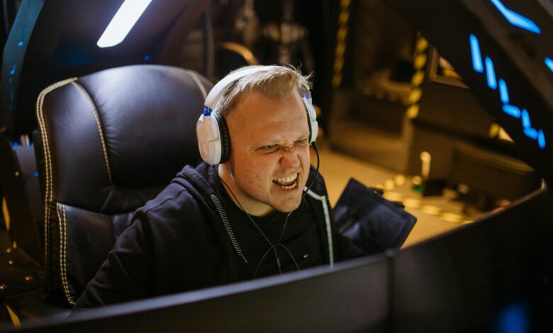 A passionate gamer celebrating victory while gaming indoors with white headphones and a gaming chair.
