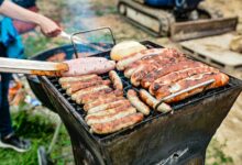 Grilling an assortment of sausages and bread at an outdoor barbecue on a sunny day.