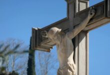 Close-up of a stone crucifix with Jesus statue against a vibrant blue sky, symbolizing faith.