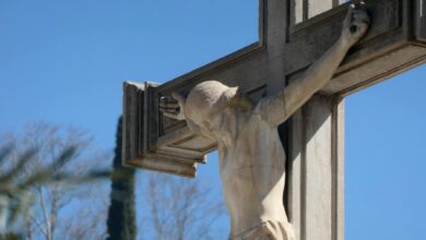 Close-up of a stone crucifix with Jesus statue against a vibrant blue sky, symbolizing faith.