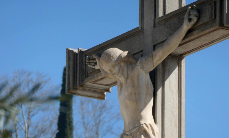 Close-up of a stone crucifix with Jesus statue against a vibrant blue sky, symbolizing faith.