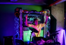 A young musician passionately plays electronic drums at an illuminated arcade setup.