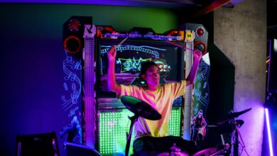 A young musician passionately plays electronic drums at an illuminated arcade setup.