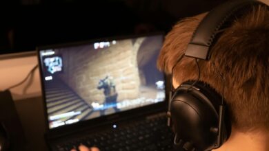 Teenage boy wearing headphones focused on playing a video game on a laptop screen indoors.