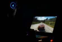 A gamer using a laptop and headphones to play a car racing game in a dark setting.
