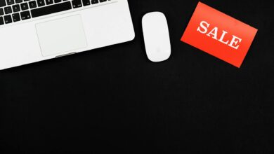Minimalist flat lay of a laptop, mouse, and a red sale sign on black background.