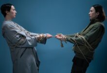 Two adults engaged in a symbolic tug of war, wrapped in rope against a blue background.