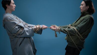 Two adults engaged in a symbolic tug of war, wrapped in rope against a blue background.
