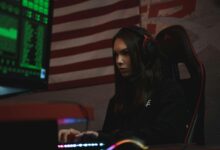 A female gamer intensely focused on her screen, wearing a headset in a dark room with neon green lighting.