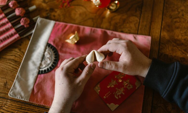 Hands holding a fortune cookie above a red envelope, symbolizing luck and tradition.