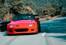 A vibrant red convertible speeds through a scenic mountain road in Sion, Switzerland, showcasing automotive elegance.