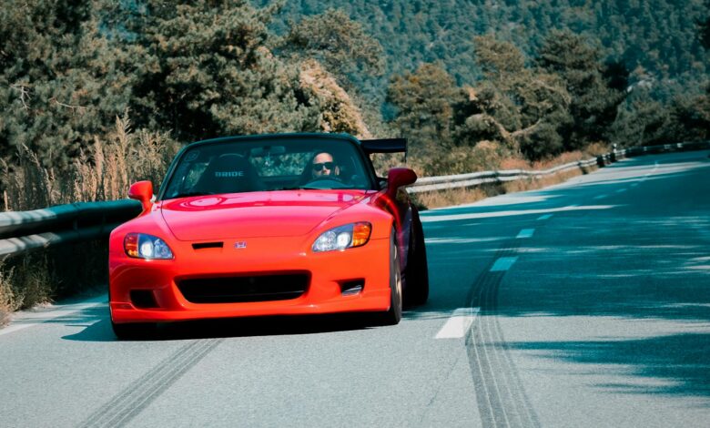 A vibrant red convertible speeds through a scenic mountain road in Sion, Switzerland, showcasing automotive elegance.