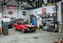 A vintage red car undergoing restoration in a well-equipped workshop with various tools and auto parts.
