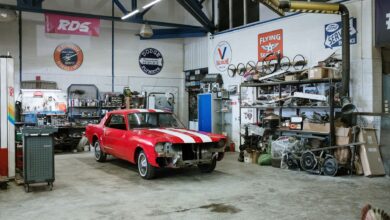 A vintage red car undergoing restoration in a well-equipped workshop with various tools and auto parts.