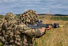 Military soldiers in camouflage gear practicing combat in a grassy countryside.