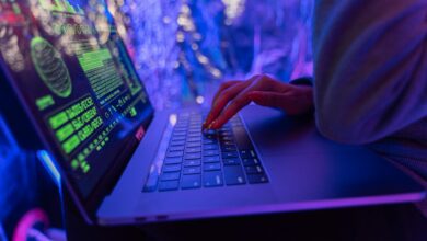 Close-up of hands typing on a laptop displaying cybersecurity graphics, illuminated by purple light.