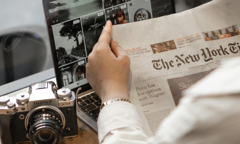 Close-up of a person reading The New York Times by a laptop and camera.