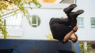 Person performing a parkour flip over a blue urban structure amidst cityscape.