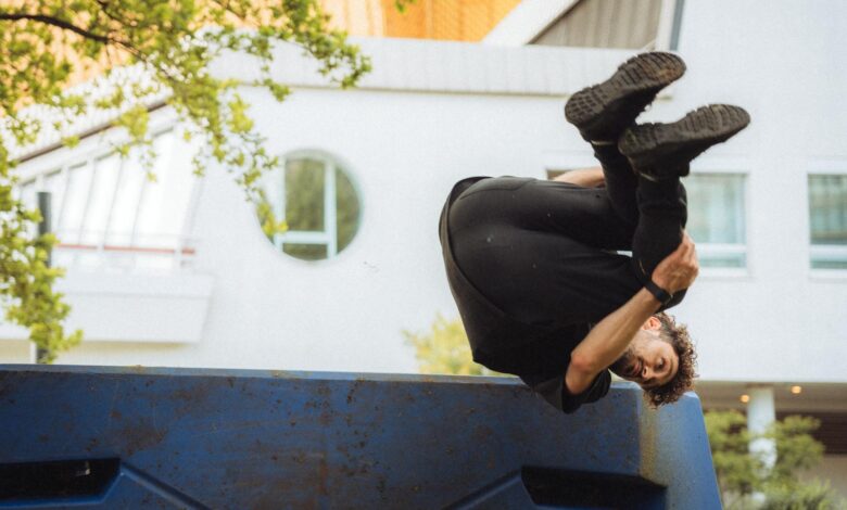 Person performing a parkour flip over a blue urban structure amidst cityscape.
