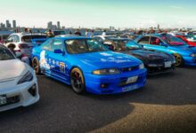 A lively outdoor car meet showcasing vibrant JDM sports cars under clear skies.