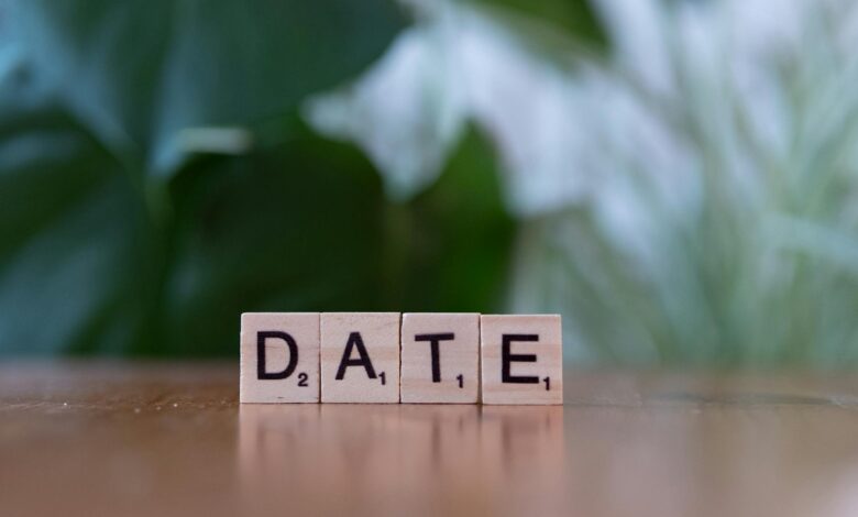 Wooden Scrabble tiles forming the word 'DATE' against a green blurred background.