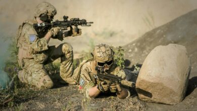 Two soldiers in camouflage uniforms practice tactical maneuvers in a desert environment, exhibiting teamwork and precision.