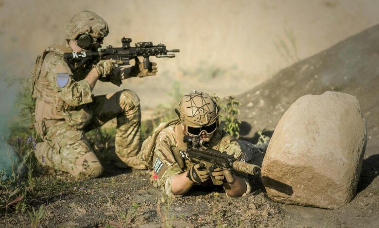 Two soldiers in camouflage uniforms practice tactical maneuvers in a desert environment, exhibiting teamwork and precision.