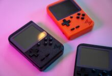A vibrant still life of retro handheld game consoles in varying colors, set against a soft background.