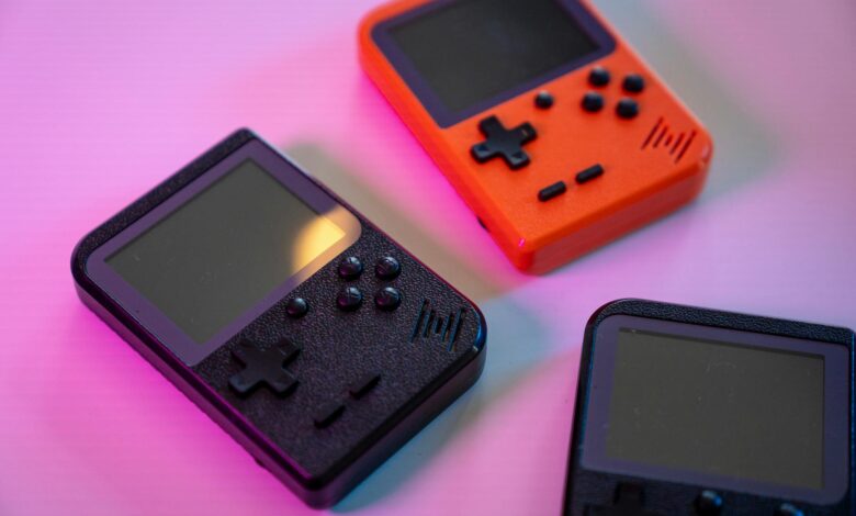 A vibrant still life of retro handheld game consoles in varying colors, set against a soft background.