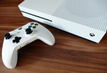 Close-up of a white Xbox console and controller on a wooden surface, ideal for gaming enthusiasts.