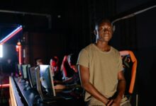 A young gamer in a dimly lit gaming arena, surrounded by teammates.