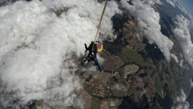 Tandem skydivers bravely descend through clouds with a parachute, capturing aerial views.