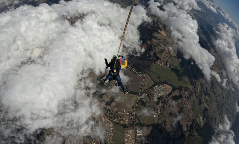 Tandem skydivers bravely descend through clouds with a parachute, capturing aerial views.