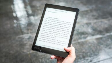A person holds an e-reader displaying text against a wet pavement background.