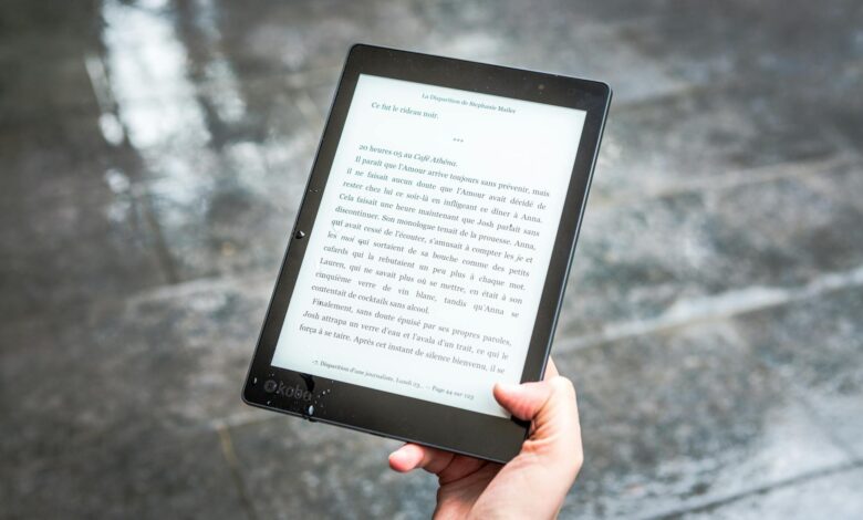 A person holds an e-reader displaying text against a wet pavement background.