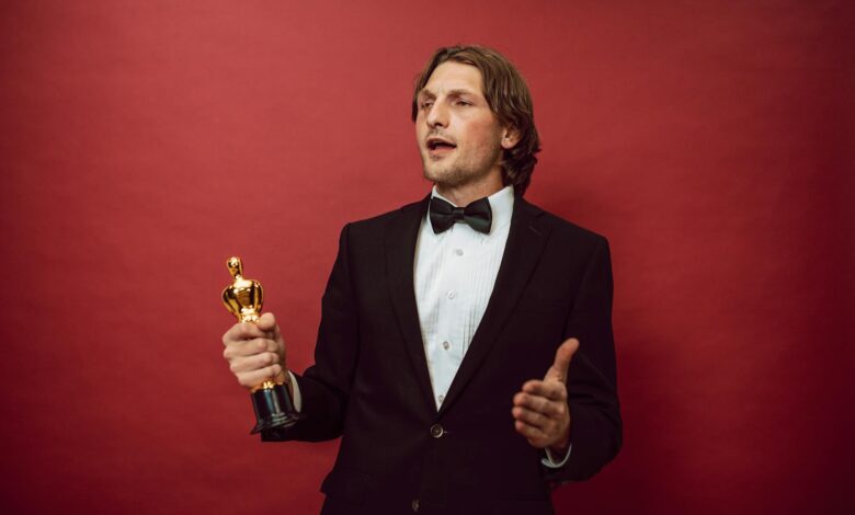 An accomplished man in a tuxedo holding a trophy, symbolizing triumph and recognition, against a red backdrop.