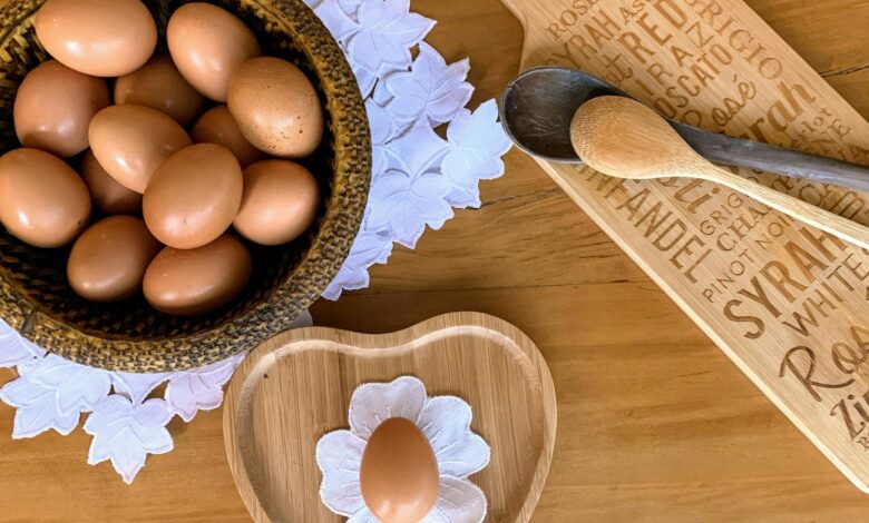 A top-down view of brown eggs in a wooden bowl, with a heart-shaped dish and utensils on a rustic table.