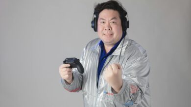Asian man with headphones celebrates while gaming, holding a controller.