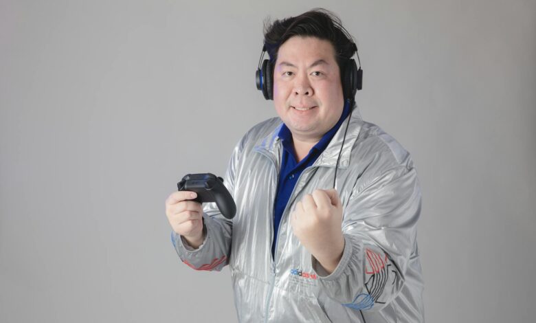 Asian man with headphones celebrates while gaming, holding a controller.