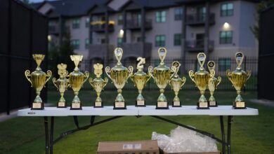 Lineup of gold trophies on a table outdoors with apartment backdrop.