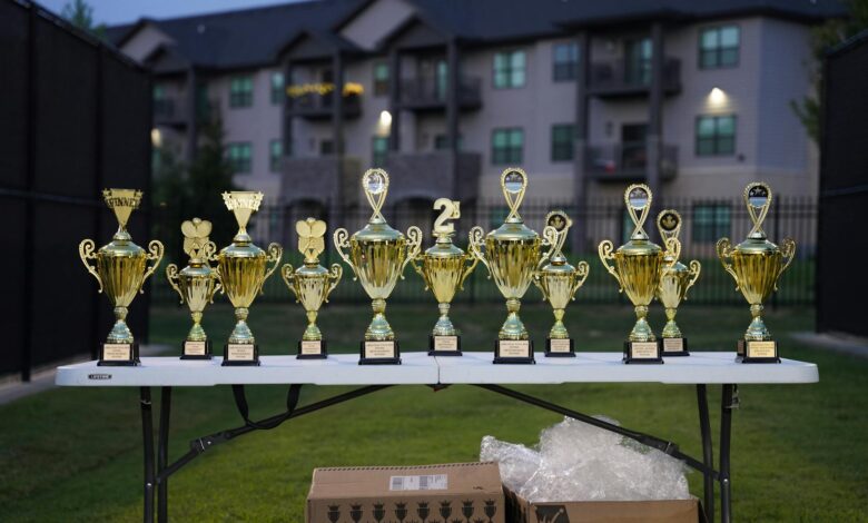 Lineup of gold trophies on a table outdoors with apartment backdrop.