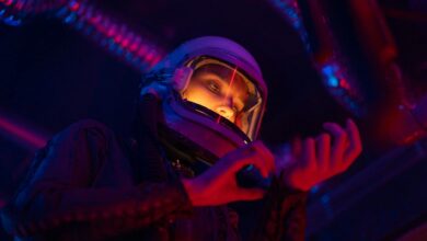 A futuristic female astronaut examines gear in vibrant colored lights.