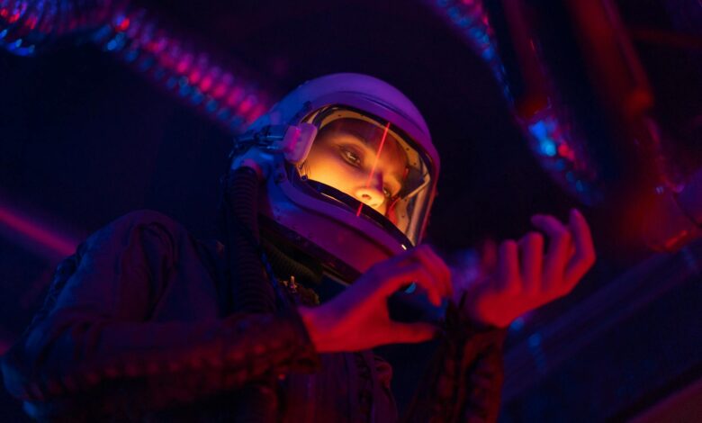 A futuristic female astronaut examines gear in vibrant colored lights.